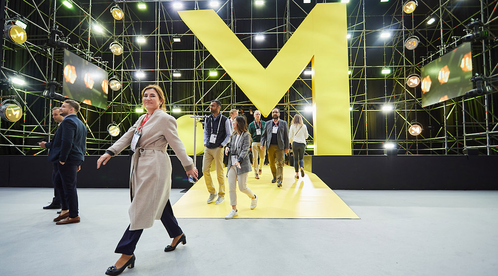 A woman smiles to camera as she enters Money20/20 Europe, with other attendees behind her.